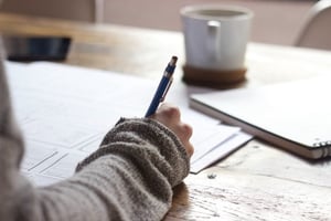 woman writing notes on paper in front of laptop during a counselling session