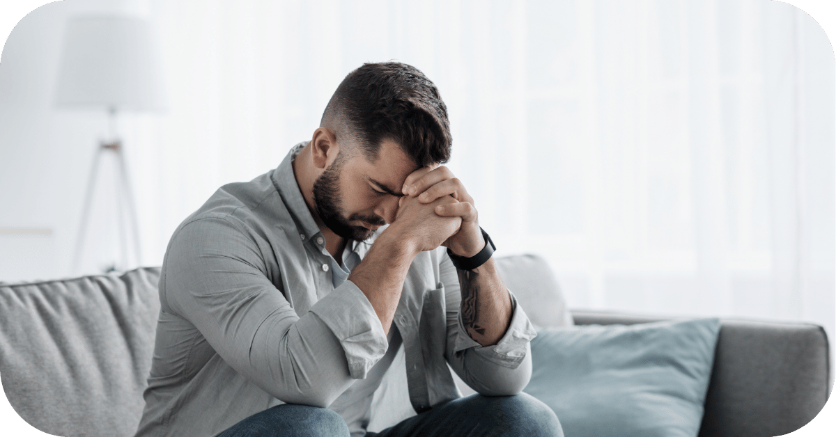 man with face in hands on couch experiencing chronic stress