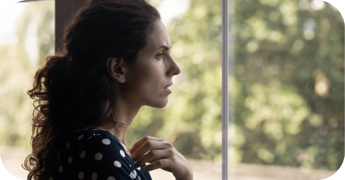 Woman feeling overwhelmed, looking out a window with a lot on her mind